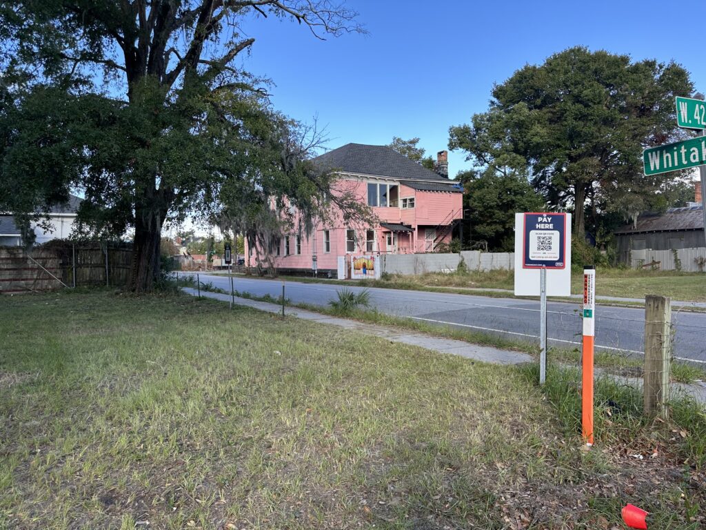 A PMC "Pay Here" parking sign with a QR code for digital payment is visible in the foreground near a road crossing.