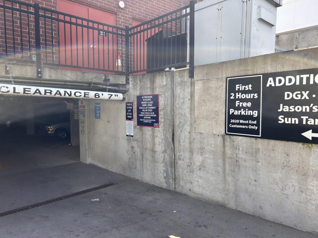 Entrance to an underground parking garage with a 6'7" clearance sign. Signs on the concrete wall advertise 2 hours of free parking for 2020 West End customers and additional parking for nearby businesses.