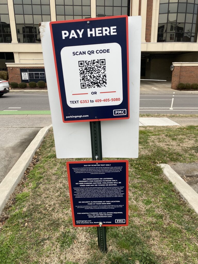 A parking sign reads "PAY HERE" with a QR code and instructions to scan it or text "G353" to a phone number for payment. Additional payment information is displayed on a smaller sign below.