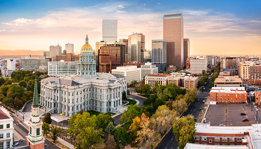 Aerial view of downtown Denver, Colorado at sunset, featuring the Colorado State Capitol building with its gold dome in the foreground and modern skyscrapers in the background.
