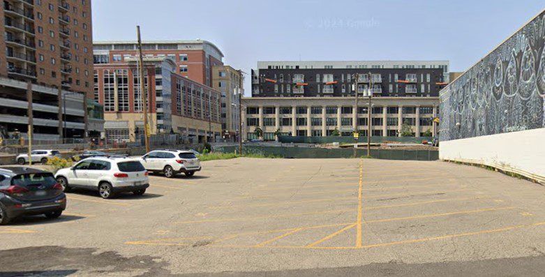 Parking Management Company parking lot with a few parked cars, surrounded by tall buildings and a large mural on the right wall.