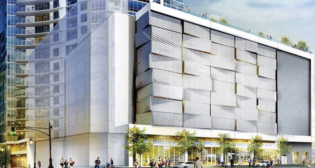 A modern multi-story building with a sleek, geometric facade features shops at street level and large windows above. People walk on the sidewalk, and some greenery is visible on the rooftop terrace.