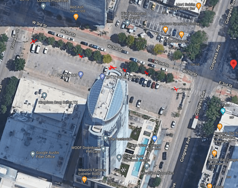 Aerial view of a city block with a tall white building, parking lots, and surrounding streets labeled like Colorado St, 3rd St, and Congress Ave. Red X marks highlight various points along the street and parking area.