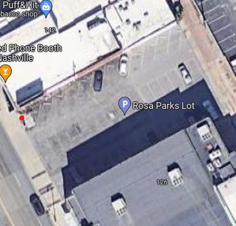 Aerial view of a parking lot labeled "Rosa Parks Lot" with parked cars and surrounding buildings in an urban area.